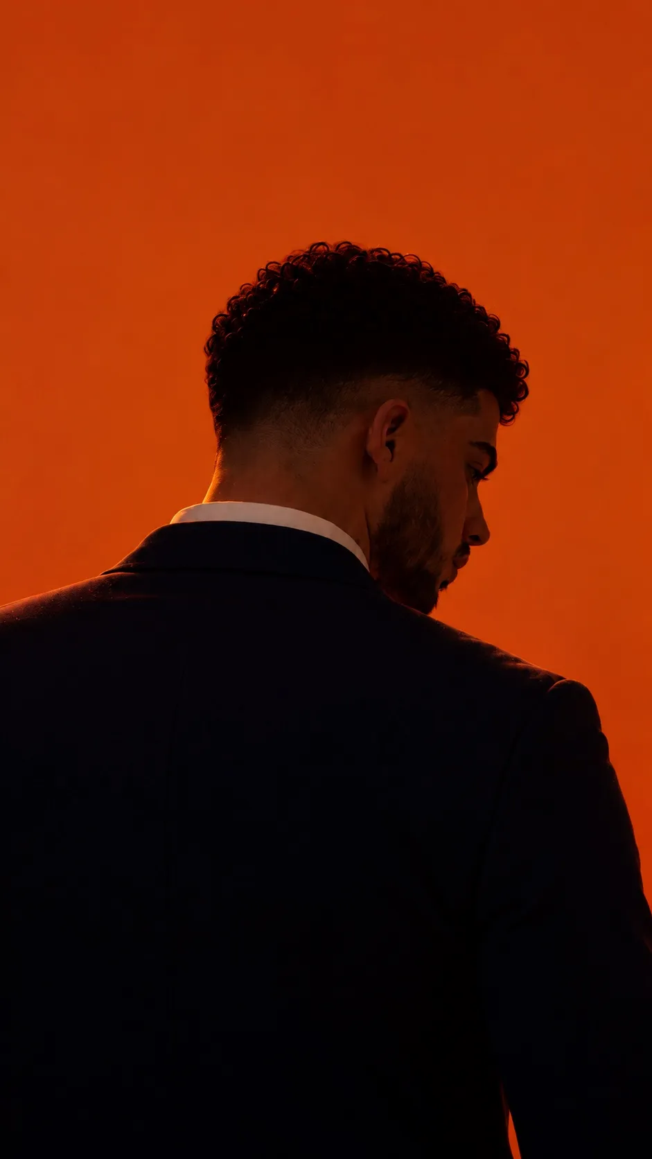 Meron, the founder of Matti Studio, seen from behind in a dark suit against an orange wall.